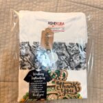 Camiseta de Ifá doblada en su empaque Ashekuba con instrucciones de lavado y tarjeta de agradecimiento