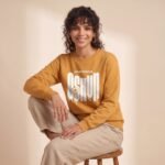 Modelo sentada con la sudadera de Oshún amarilla y pantalón de lino