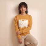 Modelo apoyada en la pared con la sudadera de Oshún amarilla